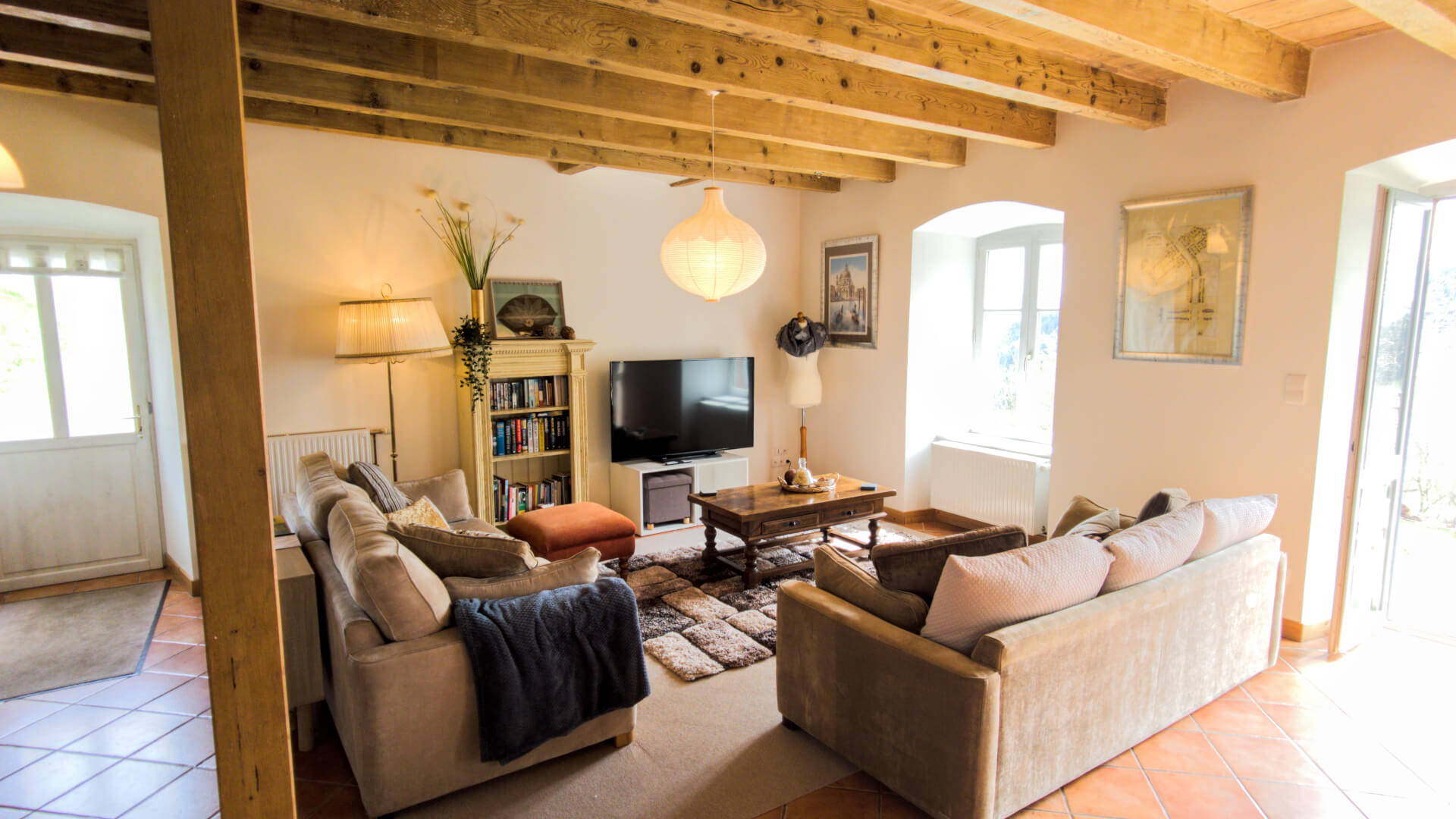 Entrez dans un salon très lumineux avec un accès à l'extérieur à droite ainsi qu'une fenêtre avec une ouverture en forme [...]